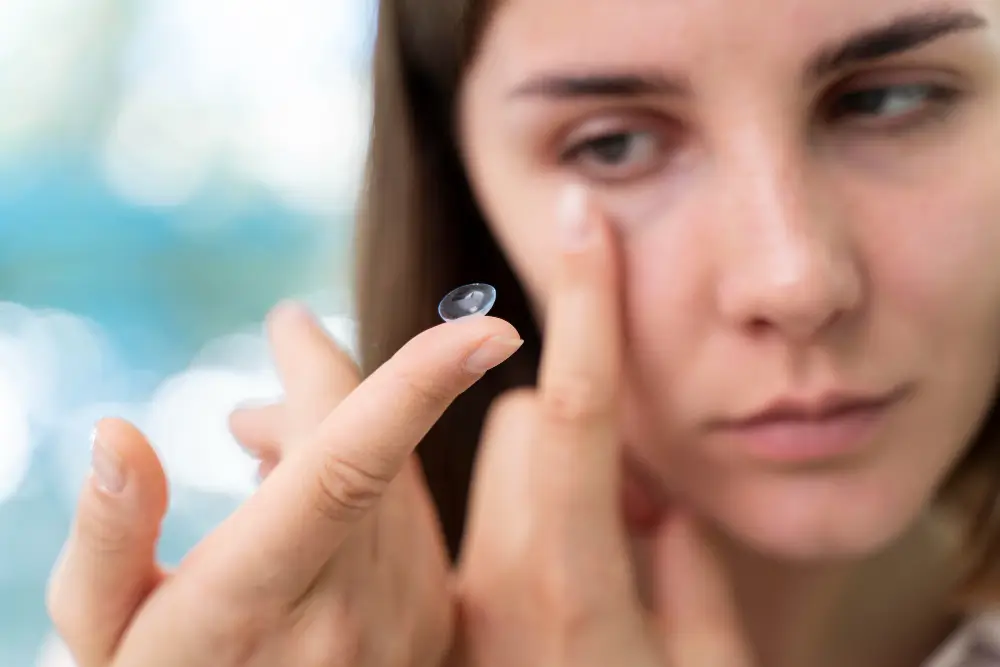 Close-up shot of a woman carefully placing a soft contact lens onto her fingertip, preparing to insert it into her eye. This image highlights the delicate process of contact lens application, crucial for preventing eye infections. Learn about contact lens eye infection symptoms you should never ignore and best practices for hygiene.
